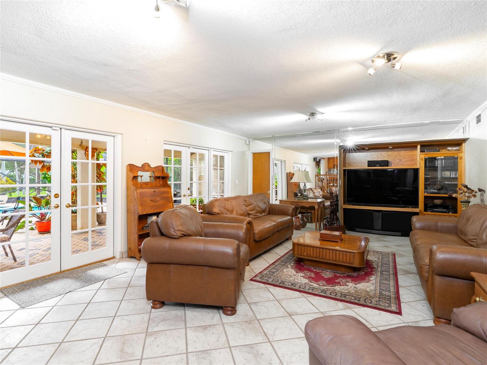 A living room features leather furniture, a tiled floor, a large media center, and glass doors — 6556 NW 87th Avenue, Parkland FL 33067, PARKLAND, FL