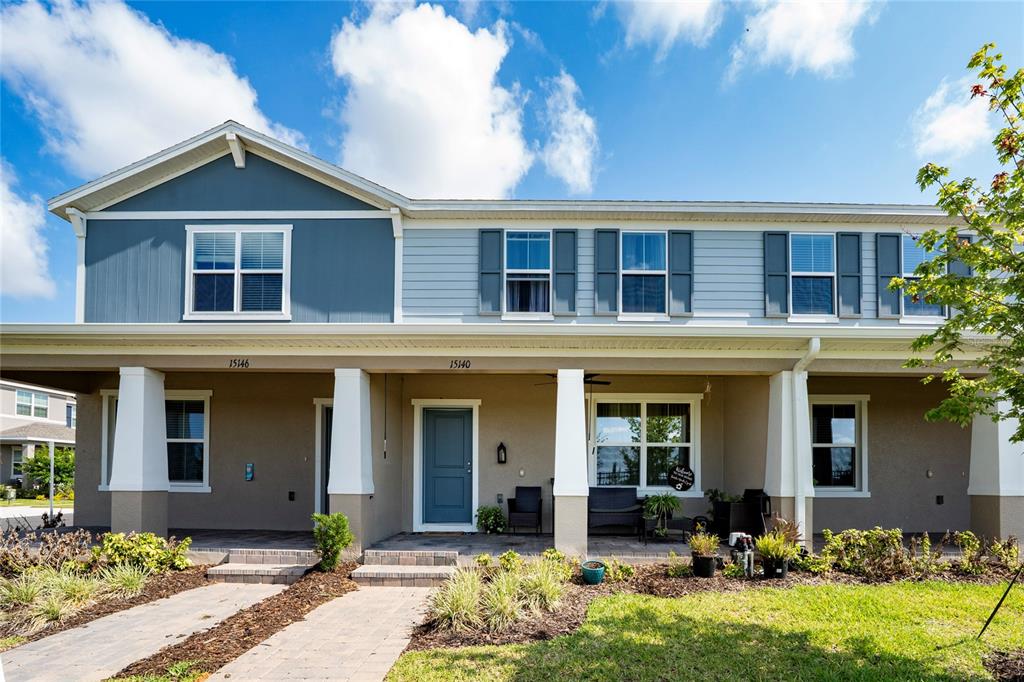 A two-story townhouse features a covered front porch, blue and beige siding, and stone accents — 15140 WINDFLOWER ALLEY, WINTER GARDEN, FL