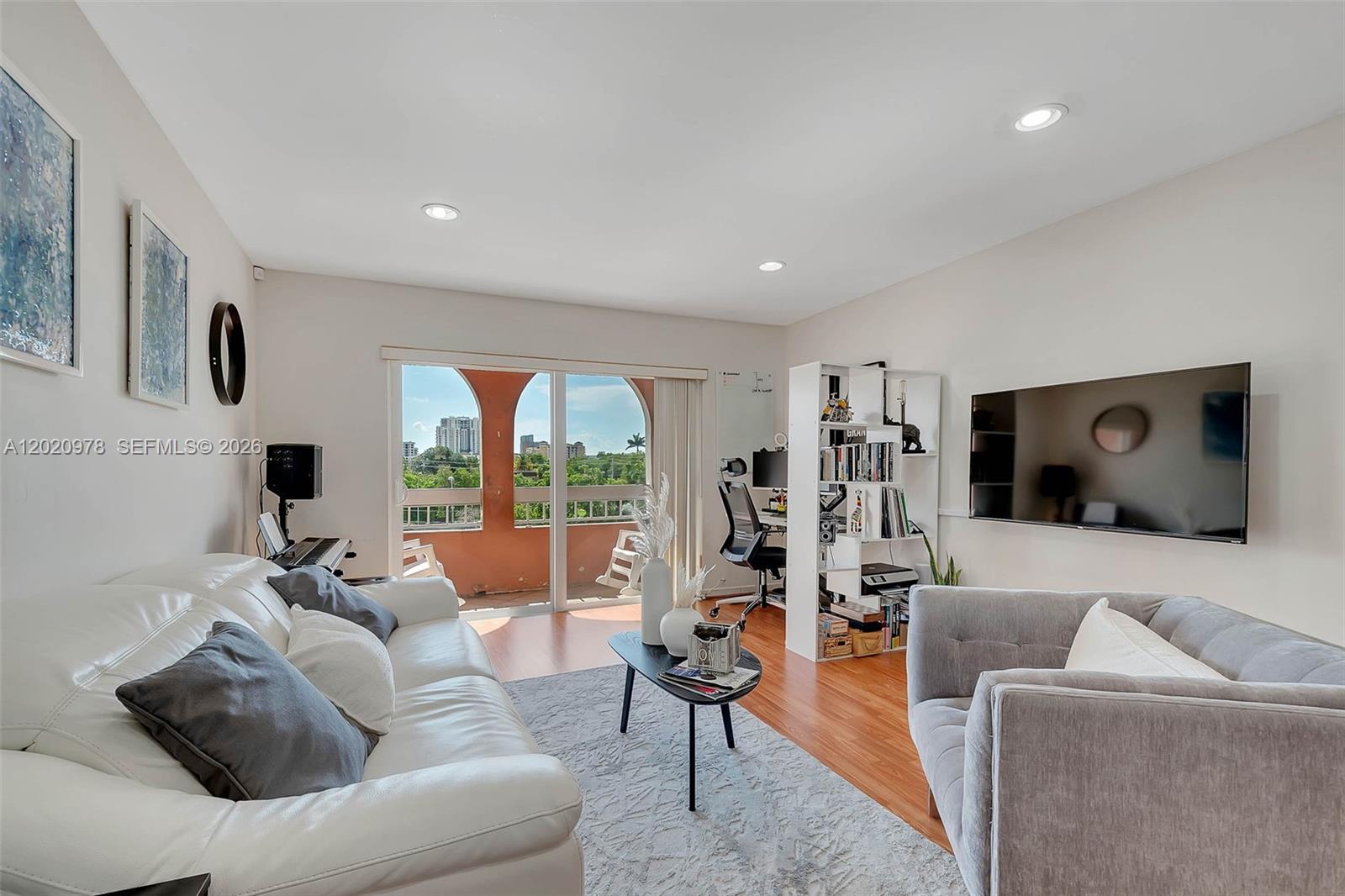 A living room features a white sofa, gray armchair, wall-mounted television, and a balcony view — 7701 Camino Real # 416, Miami FL 33143, MIAMI, FL