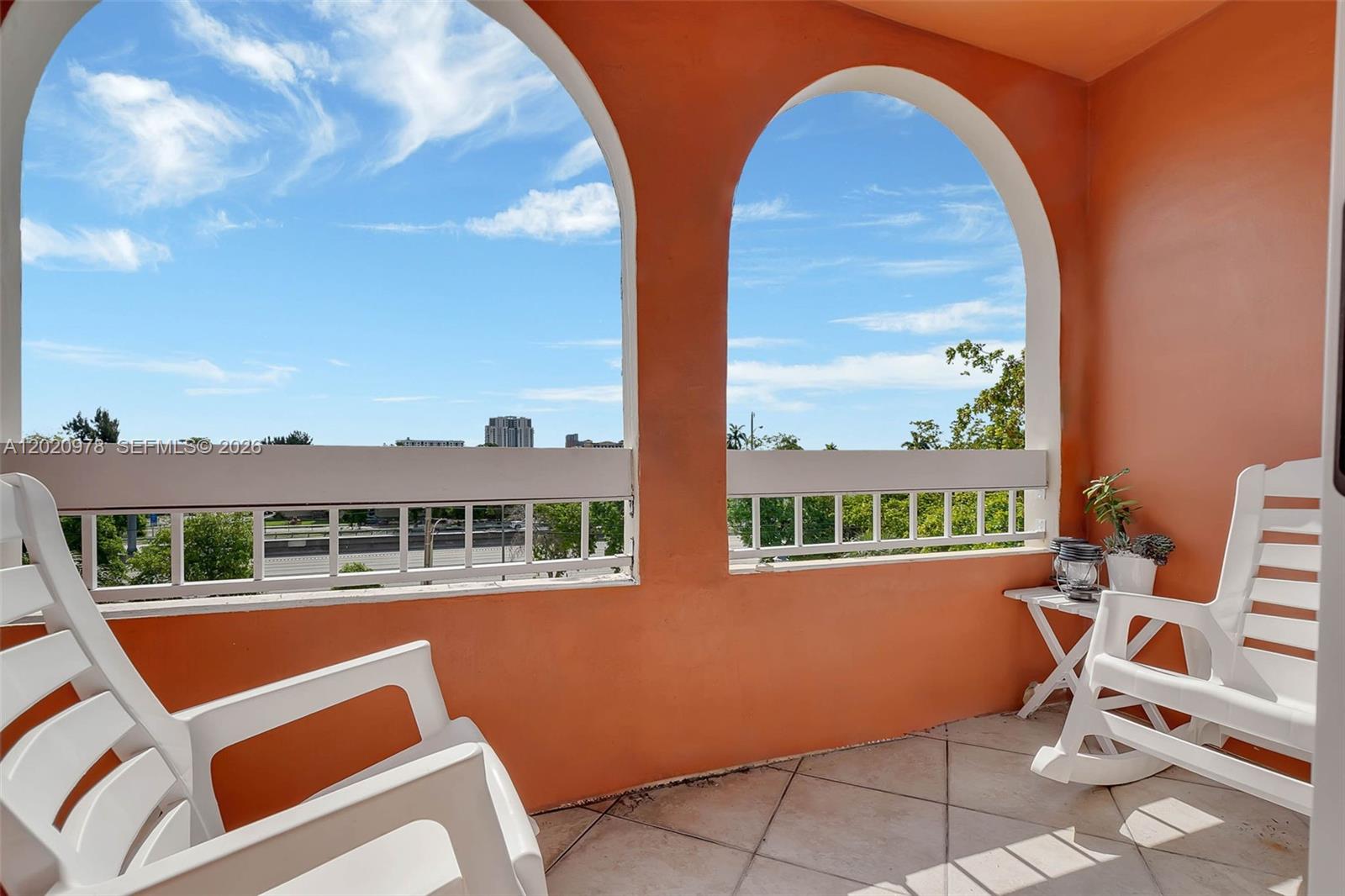 A balcony features two arched openings, white rocking chairs, and a tiled floor — 7701 Camino Real # 416, Miami FL 33143, MIAMI, FL