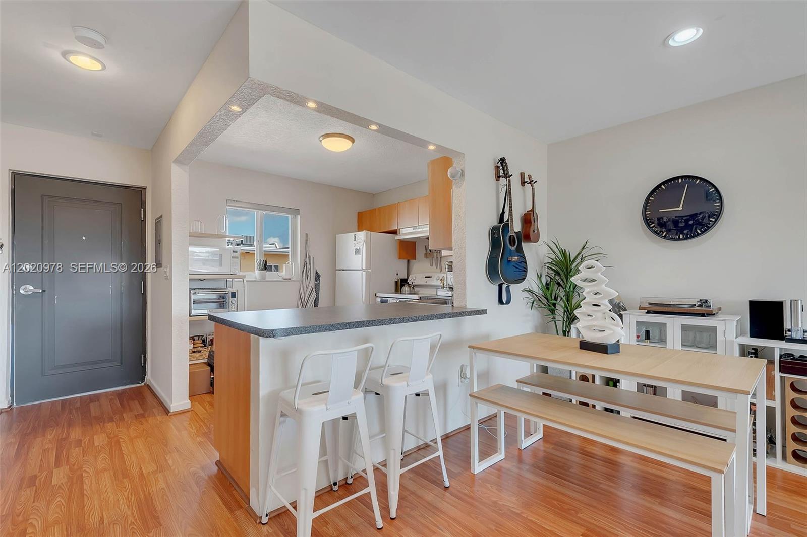 A kitchen with a breakfast bar and dining area features wood flooring and white walls — 7701 Camino Real # 416, Miami FL 33143, MIAMI, FL