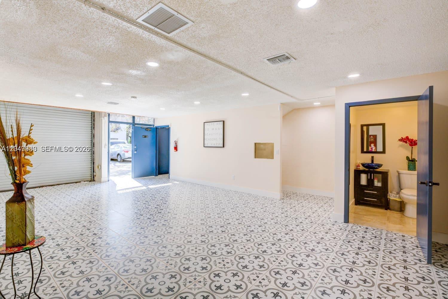 A large room with patterned tile flooring, a roll-up door, and an attached bathroom — 12349 SW 132nd Ct # 9, Miami FL 33186, MIAMI, FL