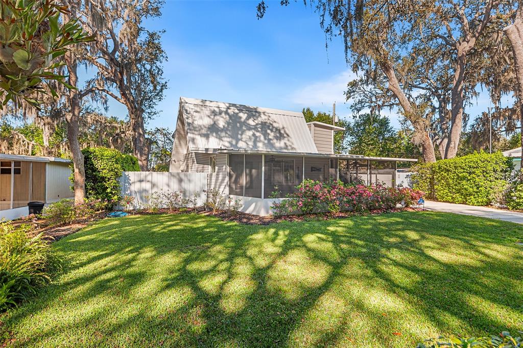 A light-colored house with a metal roof and a screened-in porch sits on a lawn — 1817 BEACHWAY LN, ODESSA, FL