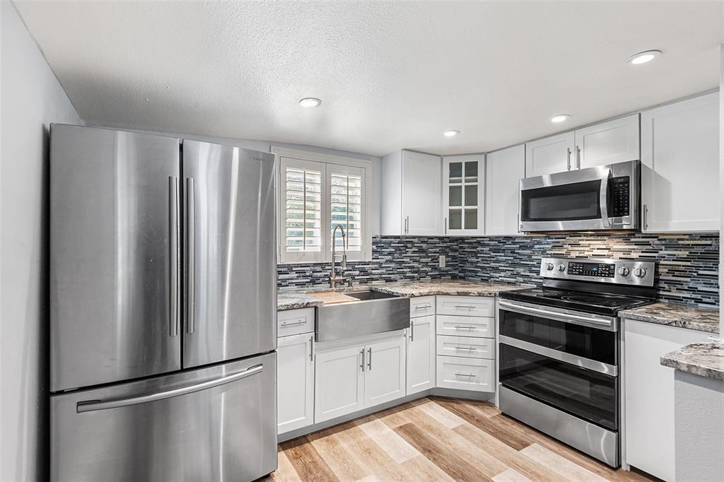 A kitchen features white cabinets, stainless steel appliances, a farmhouse sink, and a mosaic backsplash — 1817 BEACHWAY LN, ODESSA, FL