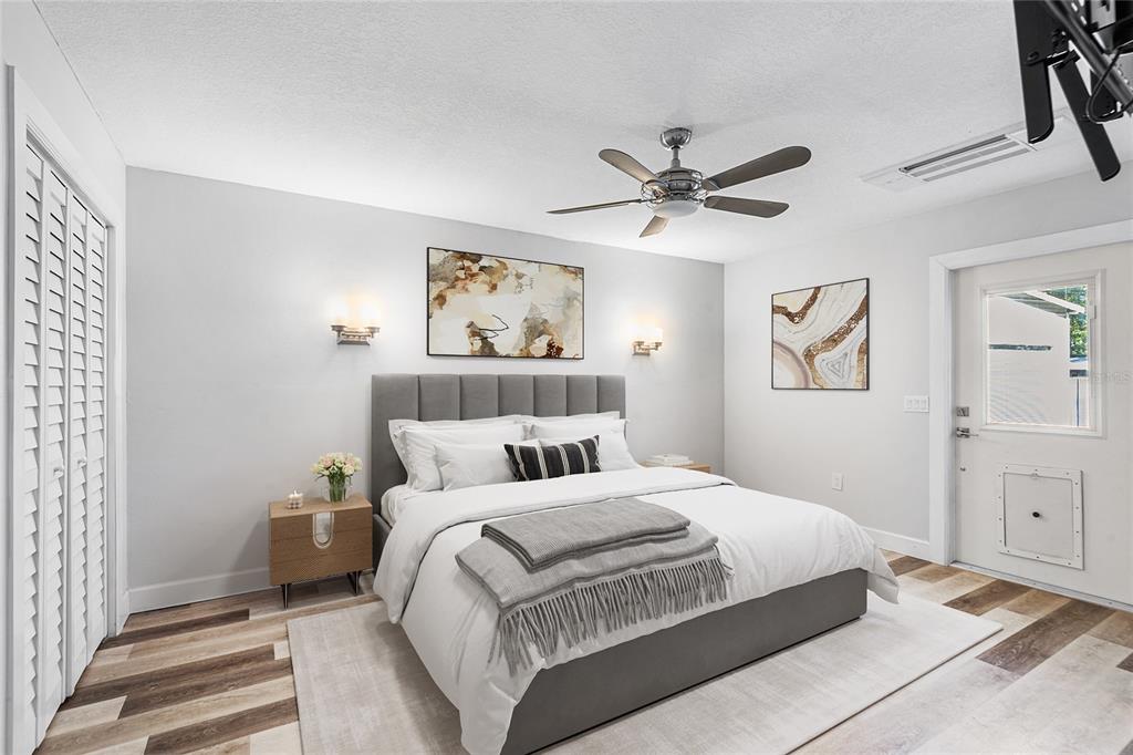 A bedroom features a gray upholstered bed, wood-look flooring, a ceiling fan, and a door — 1817 BEACHWAY LN, ODESSA, FL