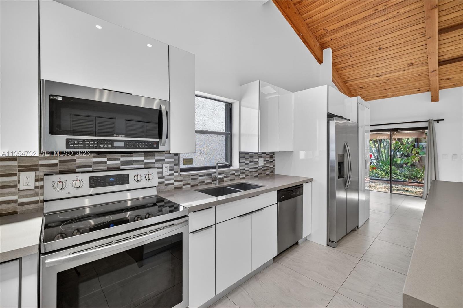 A modern kitchen features white cabinets, stainless steel appliances, a tiled backsplash, and wood-paneled ceilings — 2619 S Parkview Dr, Hallandale Beach FL 33009, HALLANDALE BEACH, FL