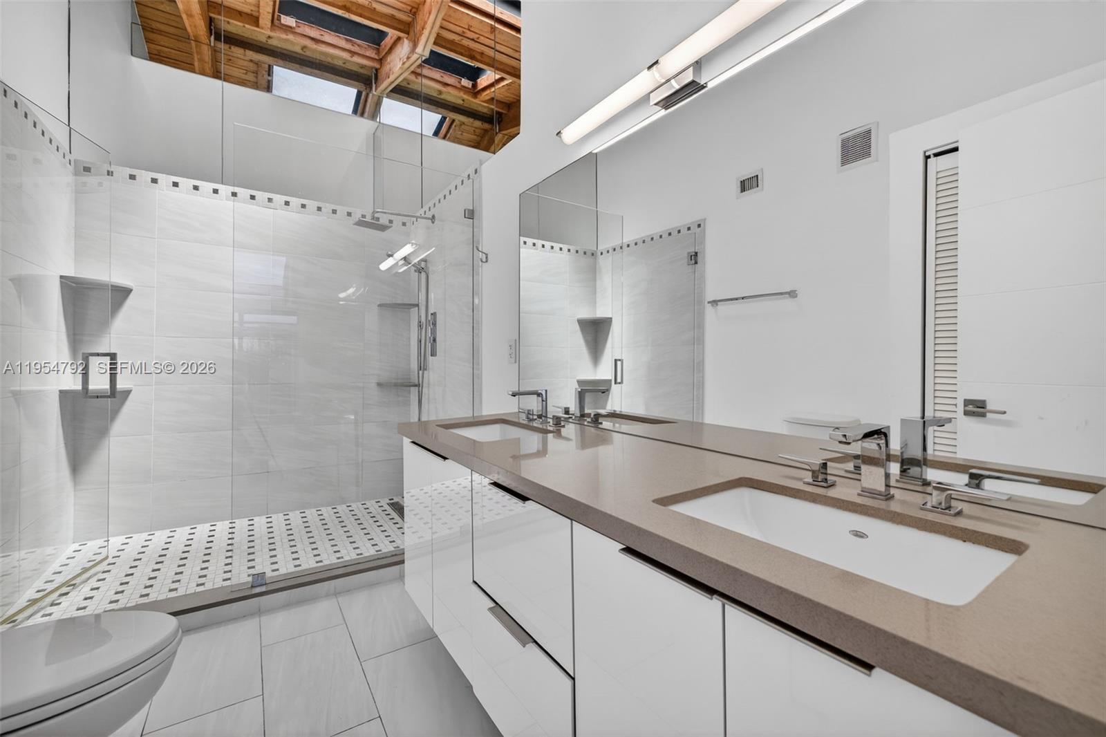 A modern bathroom features a double vanity, a glass-enclosed shower, and a vaulted wood ceiling — 2619 S Parkview Dr, Hallandale Beach FL 33009, HALLANDALE BEACH, FL