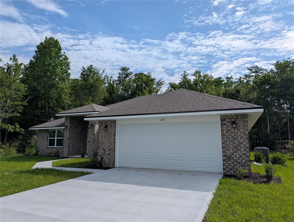 A single-story brick house with a two-car garage and a concrete driveway — 128 BIRD OF PARADISE DRIVE, PALM COAST, FL