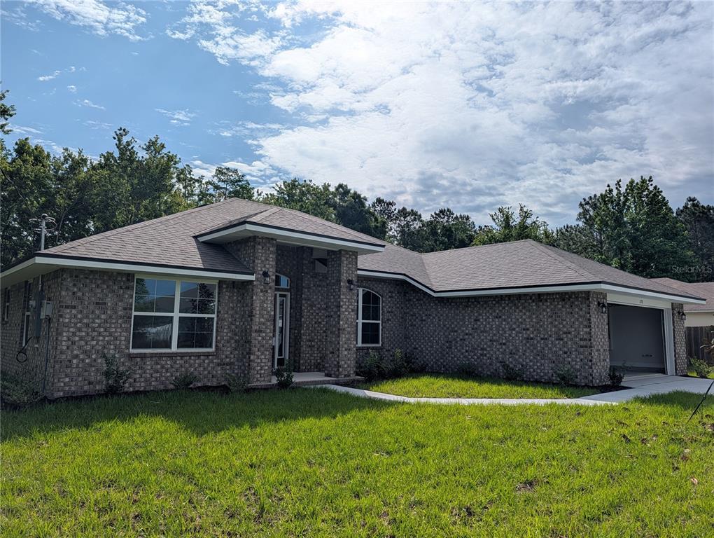 A single-story brick house with a hip roof and an attached garage under a sky — 128 BIRD OF PARADISE DRIVE, PALM COAST, FL
