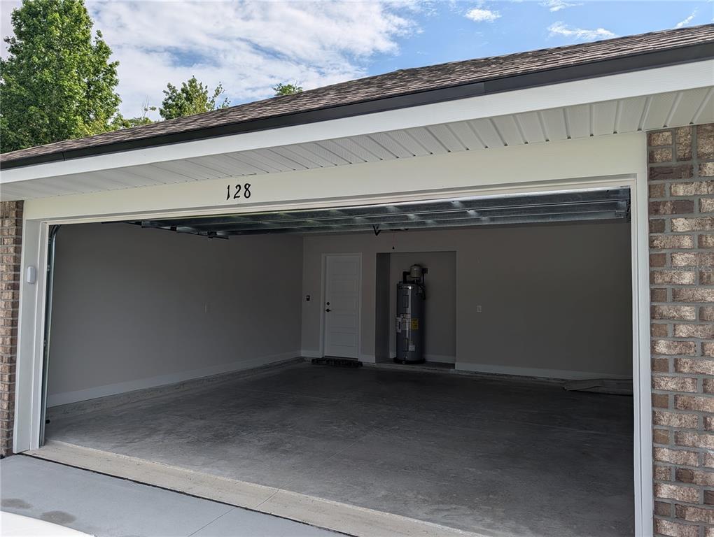An open garage with a concrete floor, a water heater, and a white door — 128 BIRD OF PARADISE DRIVE, PALM COAST, FL
