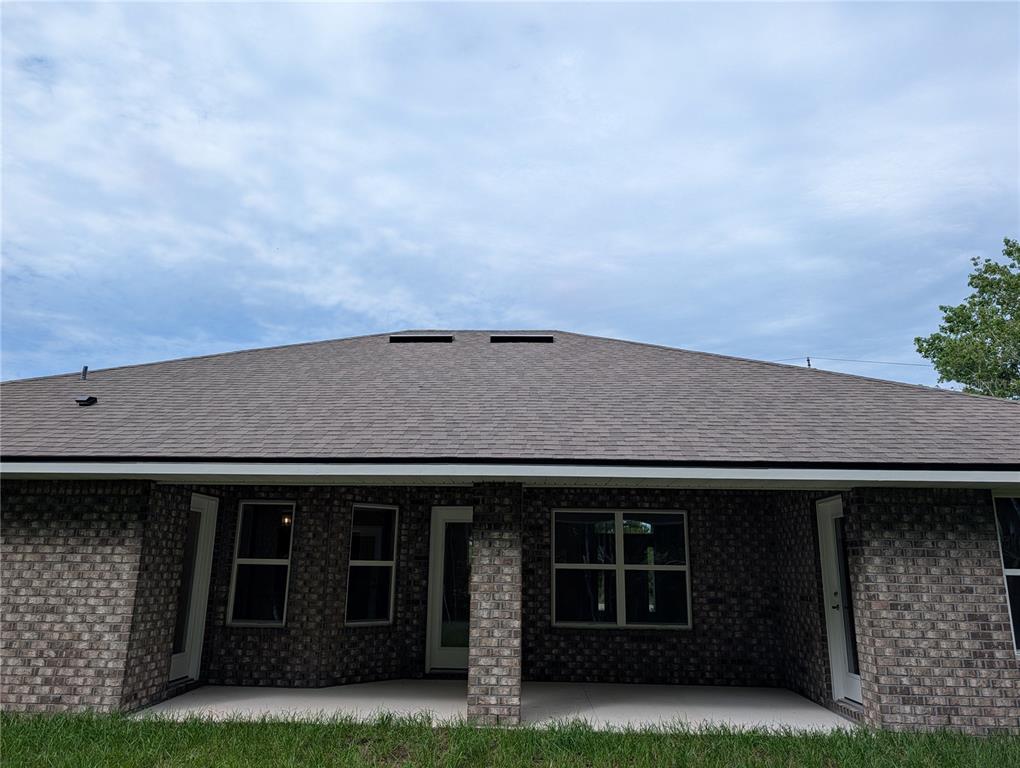 The back exterior of a brick house features a covered patio and a shingled roof — 128 BIRD OF PARADISE DRIVE, PALM COAST, FL