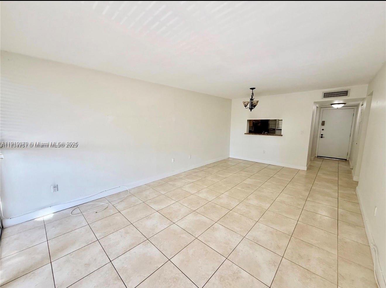 An empty living room features light-colored tile flooring, white walls, and a pass-through window — 10825 SW 112th Ave # 302, Miami FL 33176, MIAMI, FL