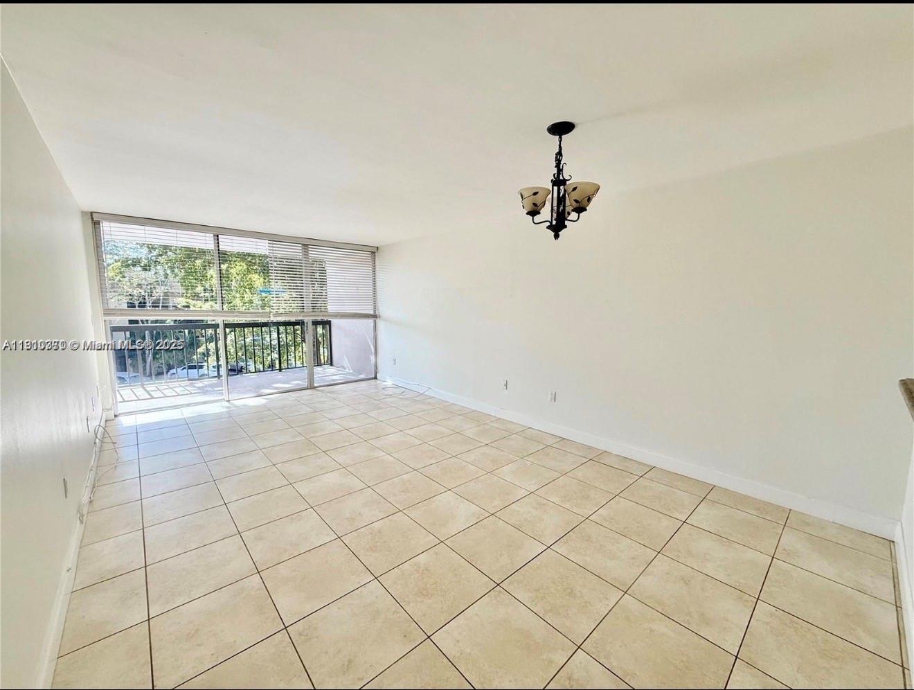 An empty room features beige tile flooring, white walls, a chandelier, and a sliding glass door — 10825 SW 112th Ave # 302, Miami FL 33176, MIAMI, FL