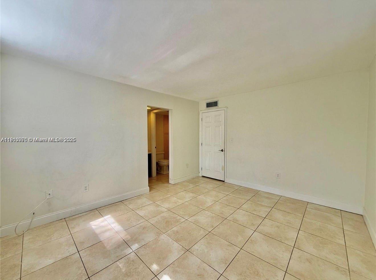 An empty room features beige tile flooring, white walls, and a doorway leading to a bathroom — 10825 SW 112th Ave # 302, Miami FL 33176, MIAMI, FL