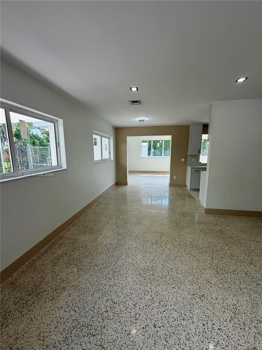 An interior view shows a room with terrazzo flooring, white walls, and a kitchen area — 8235 SW 62nd Pl, Miami FL 33143, MIAMI, FL