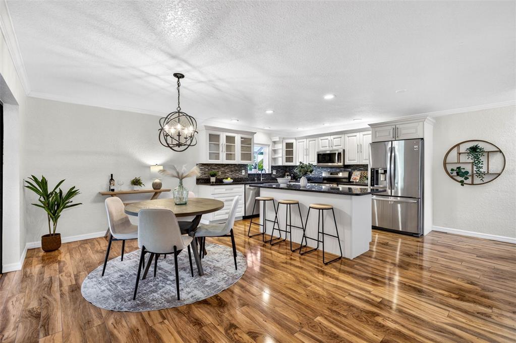 A kitchen and dining area feature white cabinets, a granite island, and wood-look flooring — 9342 TRADEWINDS AVENUE, SEMINOLE, FL