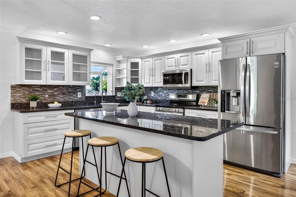 A kitchen features white cabinetry, dark granite countertops, a central island, and three bar stools — 9342 TRADEWINDS AVENUE, SEMINOLE, FL