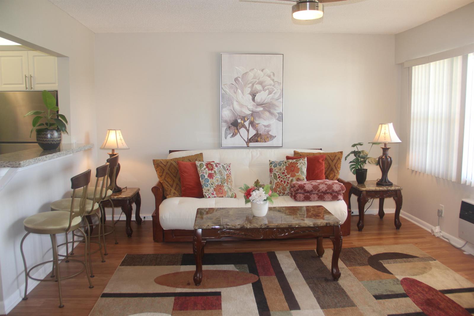 A living room with a futon, coffee table, area rug, and an open kitchen counter — 454 Fanshaw K, Boca Raton FL 33434, BOCA RATON, FL