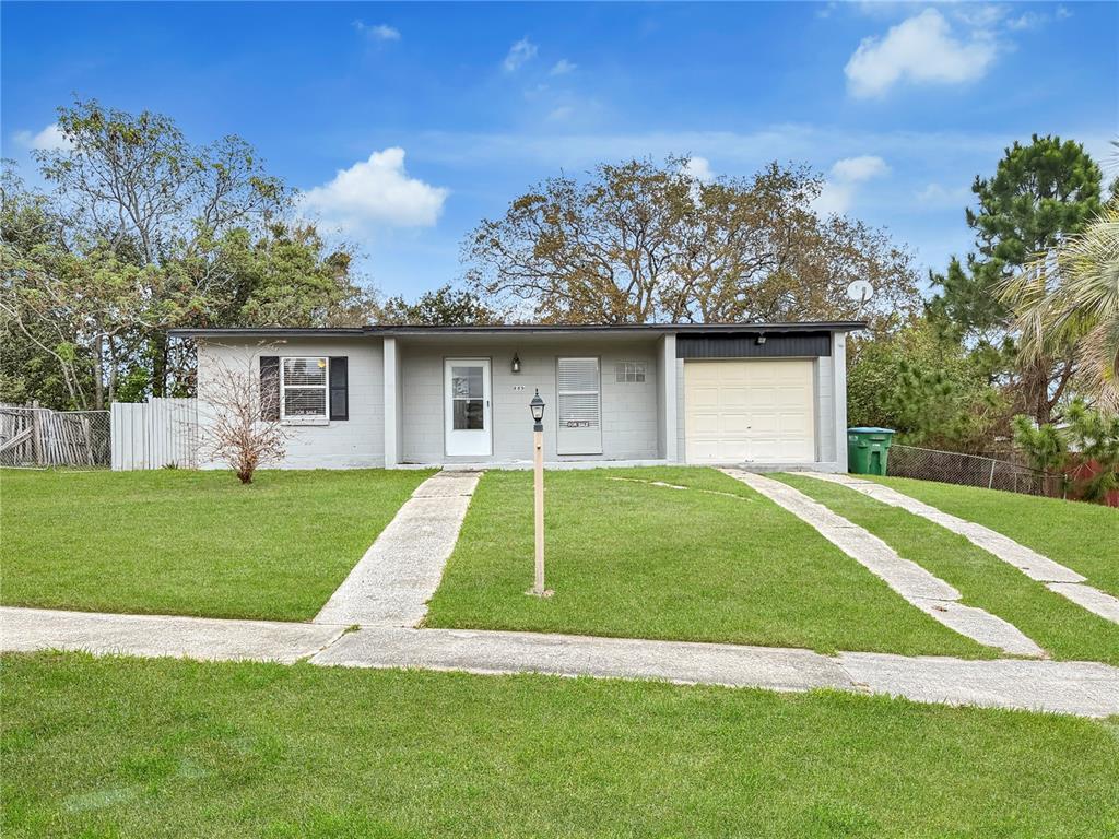 A single-story gray house with a garage and a front lawn under a blue sky — 889 W VILLAGE DRIVE, DELTONA, FL