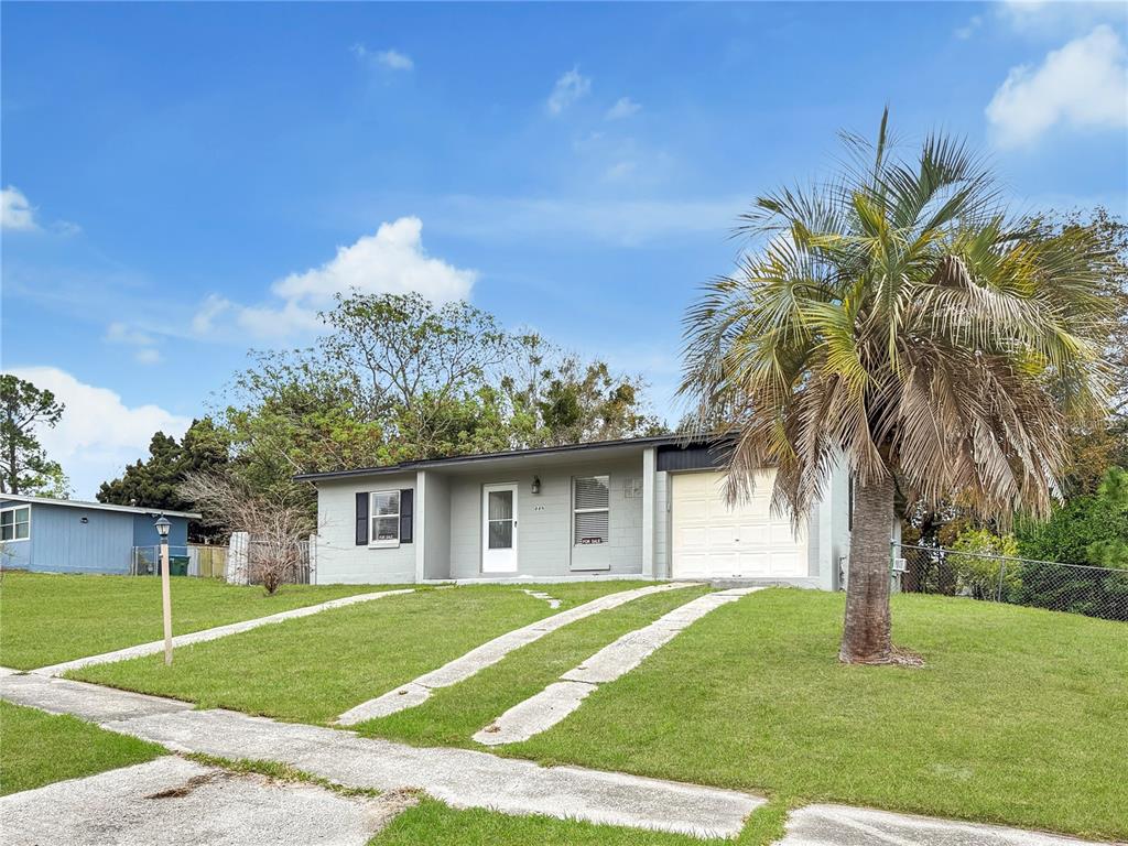A single-story house with a light gray exterior, a white garage door, and a palm tree — 889 W VILLAGE DRIVE, DELTONA, FL