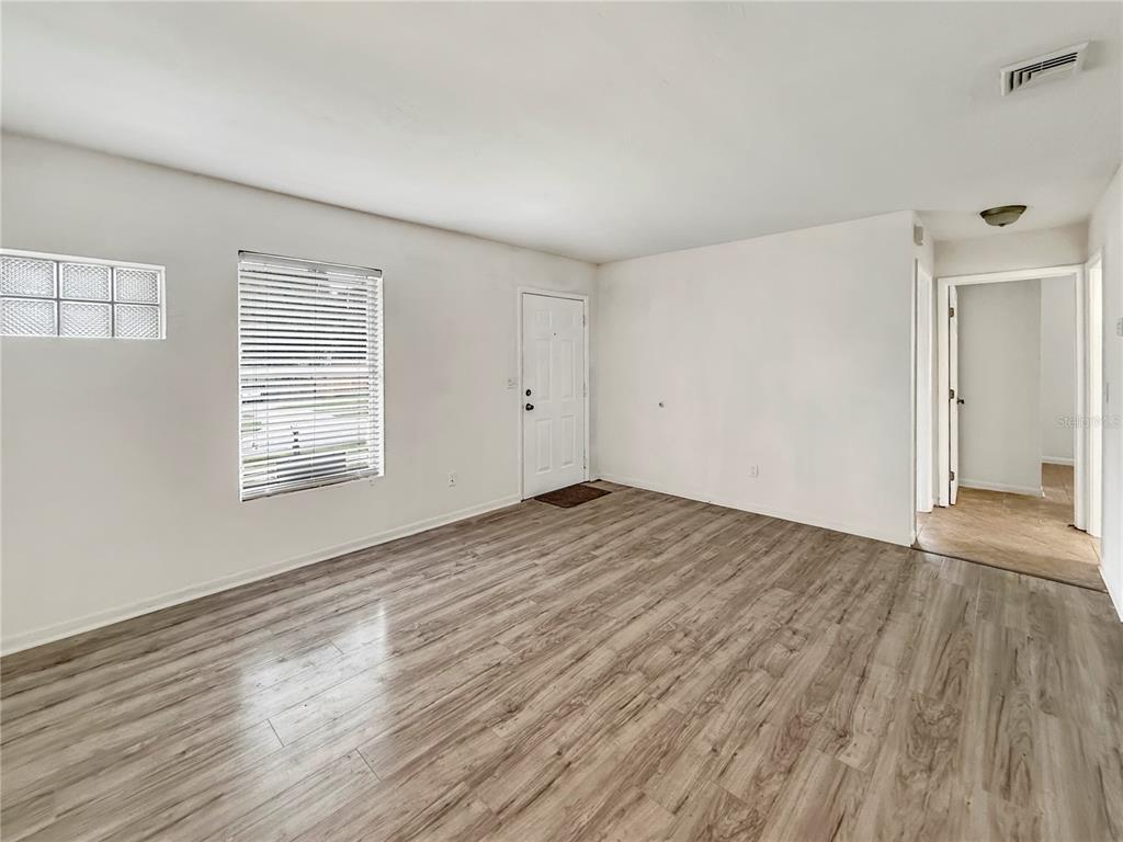 An empty living room features light wood-look flooring, white walls, a window, and a door — 889 W VILLAGE DRIVE, DELTONA, FL