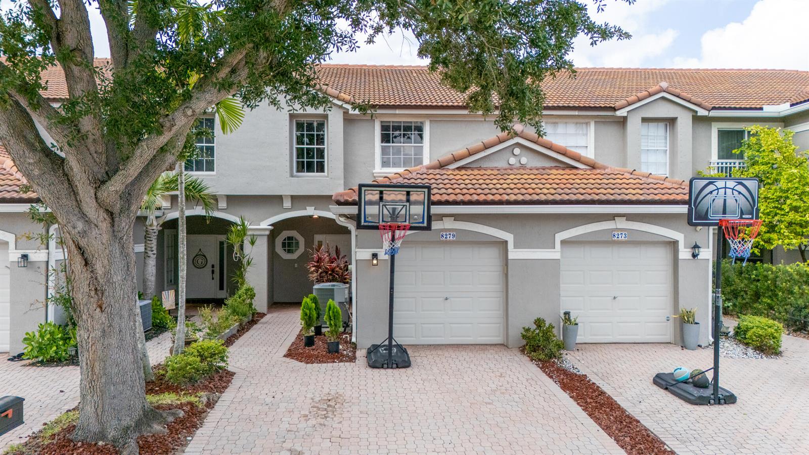 An exterior view of a two-story townhouse with two garage doors and two basketball hoops — 8279 Via Leonessa Drive, Boca Raton FL 33433, BOCA RATON, FL