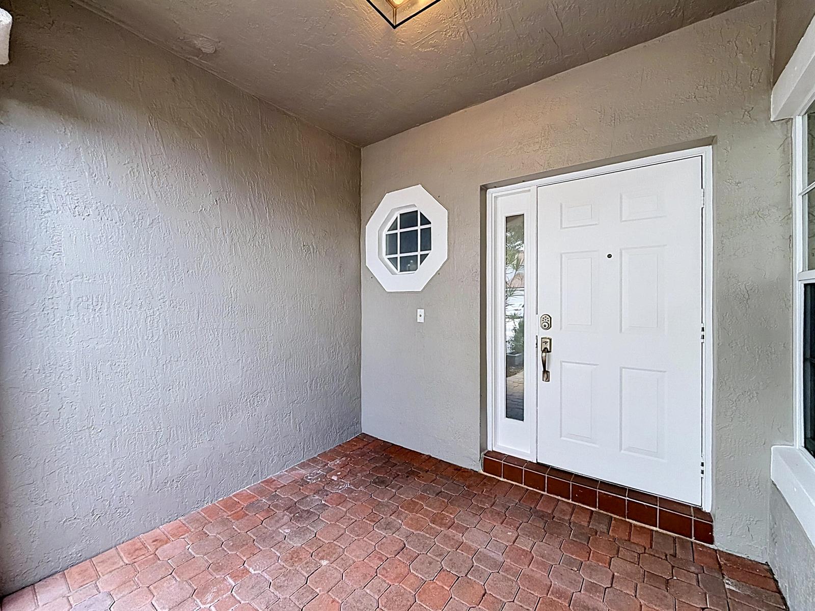 A covered entryway features a white front door with a sidelight, an octagonal window, and brick pavers — 8279 Via Leonessa Drive, Boca Raton FL 33433, BOCA RATON, FL