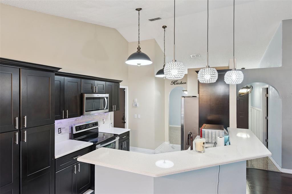 A kitchen features dark cabinetry, white countertops, a breakfast bar, and three hanging pendant lights — 907 SALERNO COURT, KISSIMMEE, FL