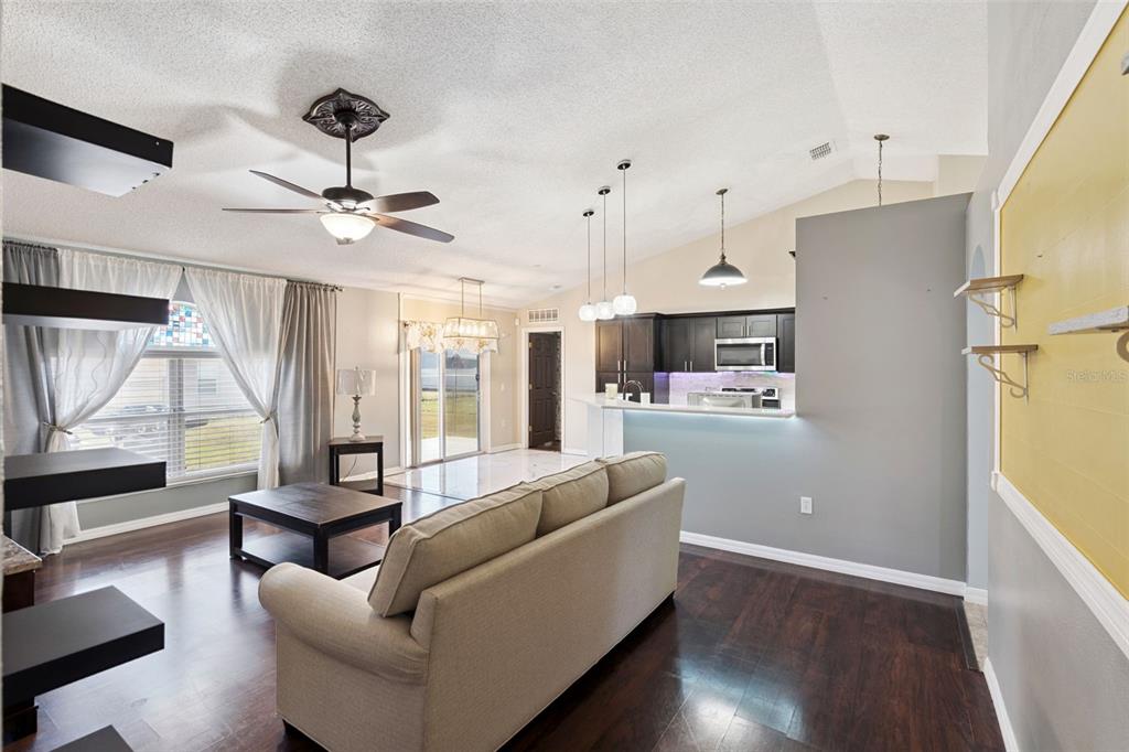 An open-concept living room and kitchen featuring dark wood floors, a sofa, and vaulted ceilings — 907 SALERNO COURT, KISSIMMEE, FL
