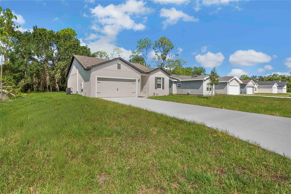 A single-story house with a beige stucco exterior, a two-car garage, and a concrete driveway — 1306 CONGO COURT, POINCIANA, FL