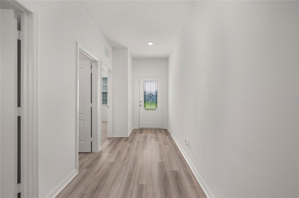 A hallway with light wood-look flooring leads to a white front door with glass inserts — 1306 CONGO COURT, POINCIANA, FL