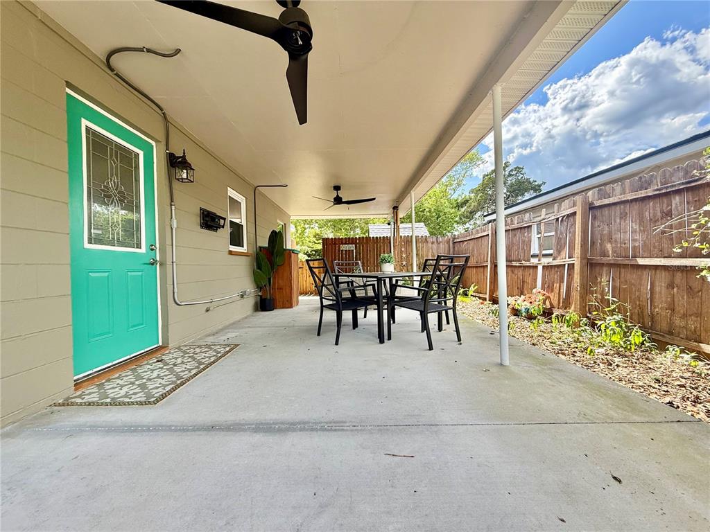 A covered concrete patio features a teal door, outdoor dining set, and wooden privacy fence — 2440 ANASTASIA DRIVE, SOUTH DAYTONA, FL