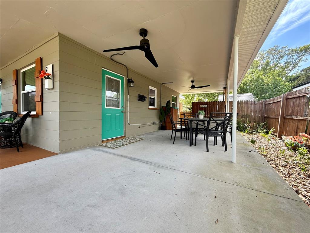 A covered concrete patio features a teal door, outdoor dining furniture, and ceiling fans — 2440 ANASTASIA DRIVE, SOUTH DAYTONA, FL