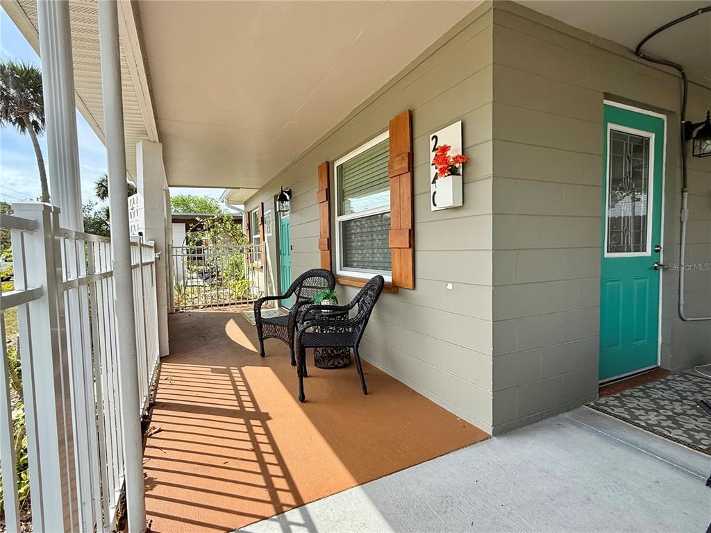 A covered porch features two black wicker chairs, a teal door, and light-colored siding — 2440 ANASTASIA DRIVE, SOUTH DAYTONA, FL