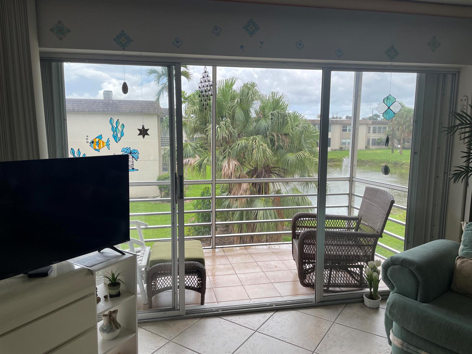 A living room looks out through sliding glass doors onto a screened balcony with water views — 506 Davis Road # 78, Palm Springs FL 33461, PALM SPRINGS, FL