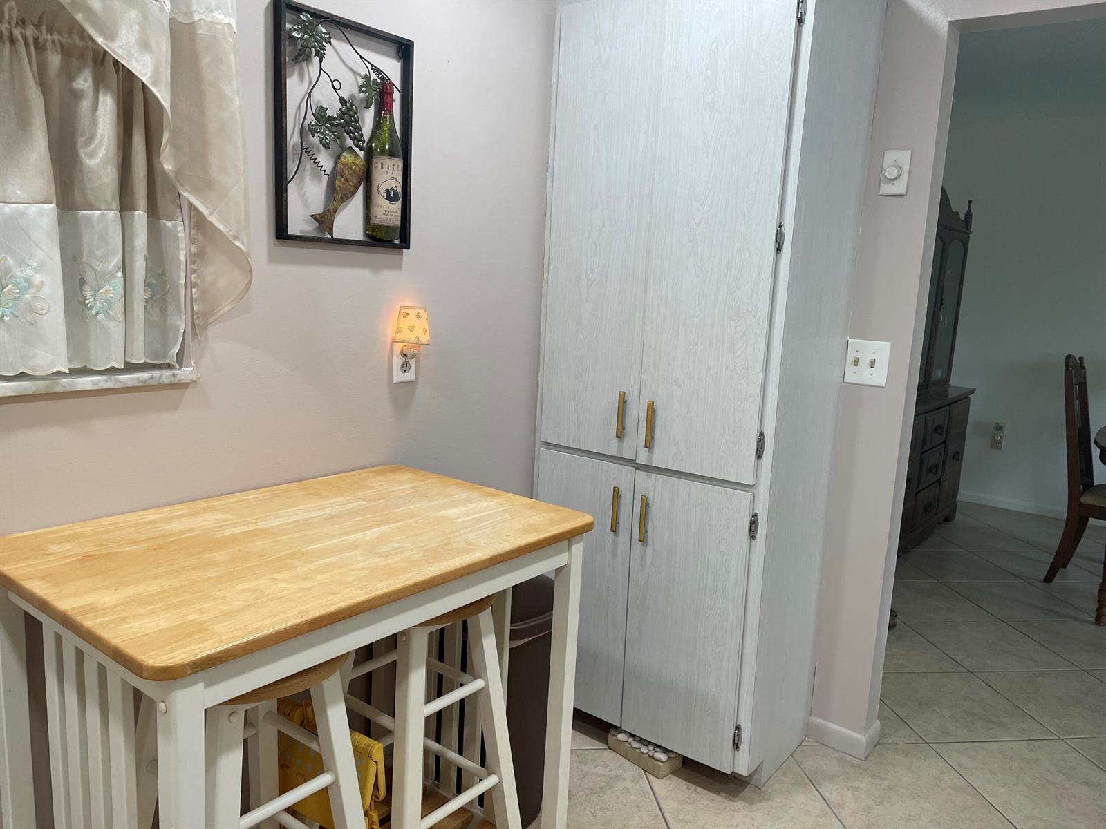 A kitchen area features a wooden table with stools, a tall pantry cabinet, and wall decor — 506 Davis Road # 78, Palm Springs FL 33461, PALM SPRINGS, FL