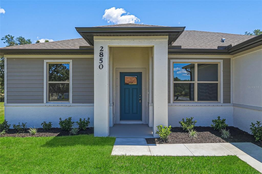 The exterior of a single-story house features a blue front door and tan siding — 2850 ESCAMBIA CIRCLE, NORTH PORT, FL