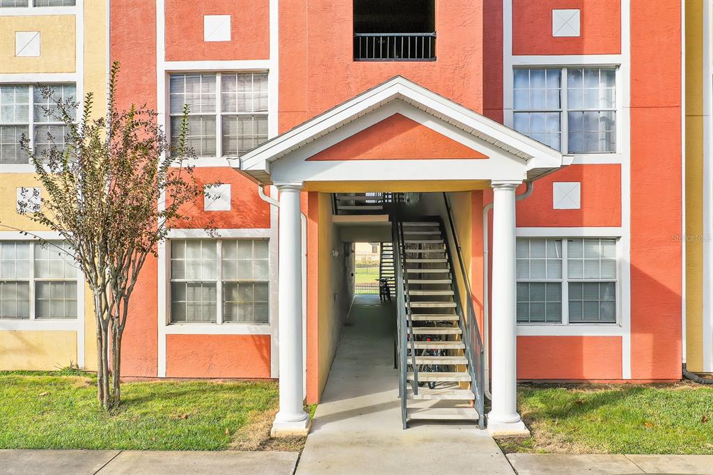 Exterior view of an apartment building entrance with a covered staircase and white columns — 10873 WINDSOR WALK DRIVE UNIT 4106, ORLANDO, FL