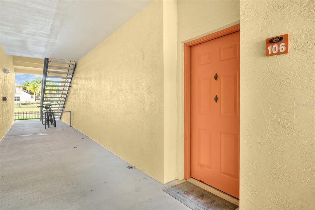 An orange front door labeled 106 sits under a covered walkway next to metal stairs — 10873 WINDSOR WALK DRIVE UNIT 4106, ORLANDO, FL