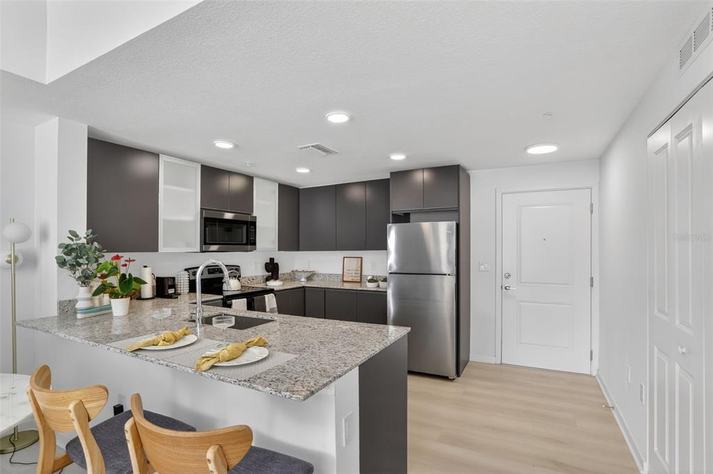 A modern kitchen features dark cabinetry, granite countertops, stainless steel appliances, and a breakfast bar — 5579 MILLENIA PARK BOULEVARD UNIT 101, ORLANDO, FL