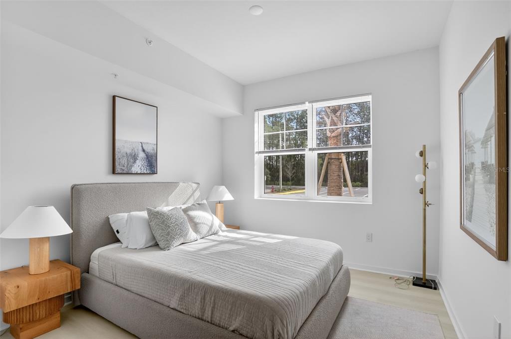 A bedroom features a gray upholstered bed, two wooden nightstands with lamps, and a window — 5579 MILLENIA PARK BOULEVARD UNIT 101, ORLANDO, FL