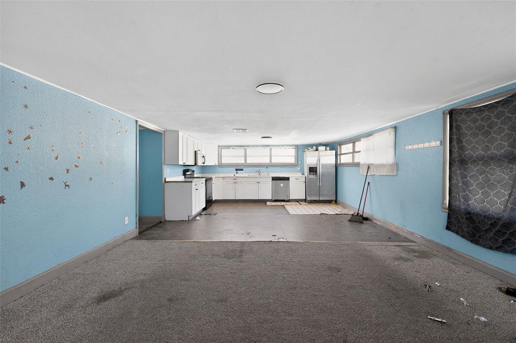 A kitchen with white cabinets and stainless appliances opens into a carpeted living area — 108 EARL AVENUE, AUBURNDALE, FL