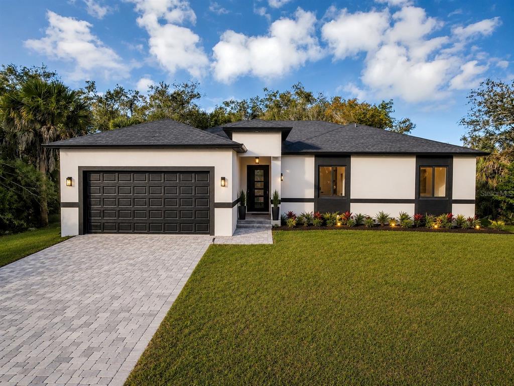 A single-story house with a black garage door, white stucco walls, and a paved driveway — 493 SYCAMORE, PORT CHARLOTTE, FL