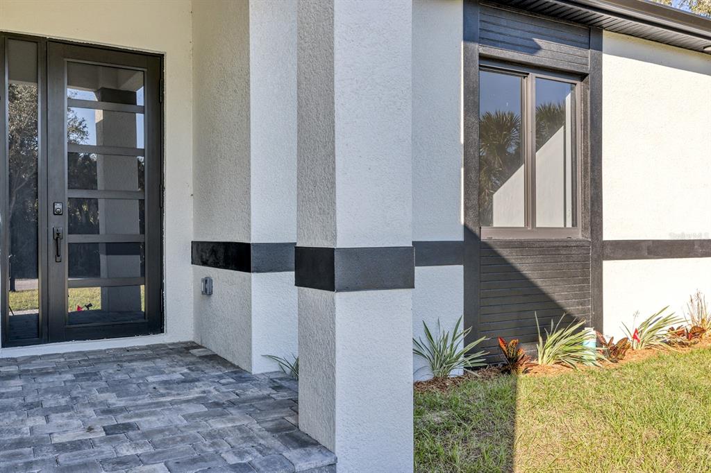 A modern home exterior features a glass-paneled front door, stone porch, and dark trim — 493 SYCAMORE, PORT CHARLOTTE, FL