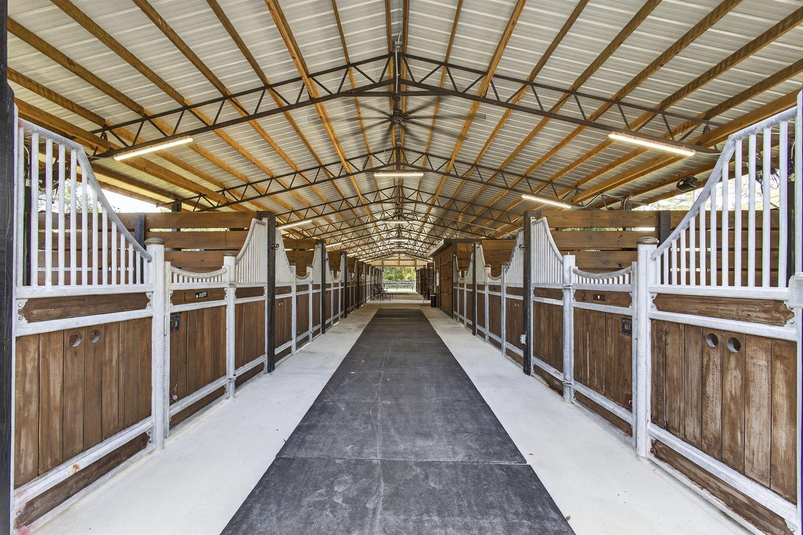 A central aisle leads through a horse barn with wooden stalls and a metal roof — 14346 Tripp Road N, FL 33470, FL