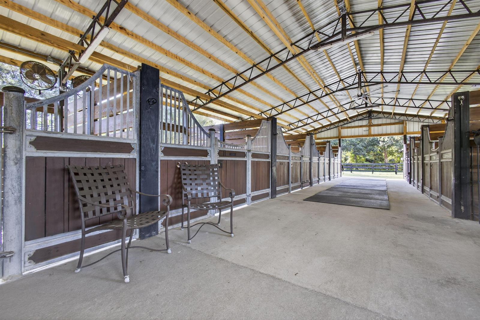 An open-air horse barn features a concrete aisle, metal roof, and several wooden stalls — 14346 Tripp Road N, FL 33470, FL