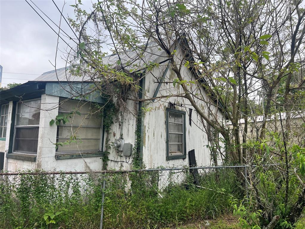 An exterior view of a weathered, white-sided house partially obscured by overgrown trees and vines — 11760 N WILLIAMS STREET, DUNNELLON, FL