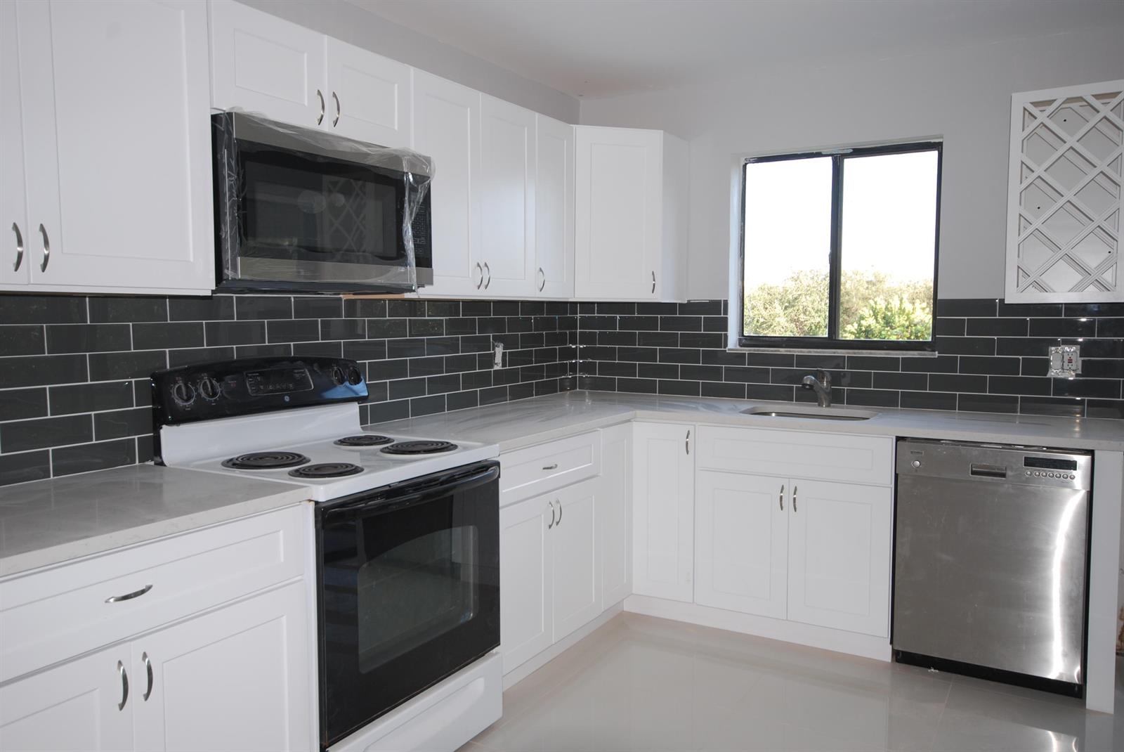 A kitchen features white cabinets, stainless steel appliances, dark subway tile backsplash, and light countertops — 5917 Via Vermilya # 308, Lake Worth FL 33462, LAKE WORTH, FL