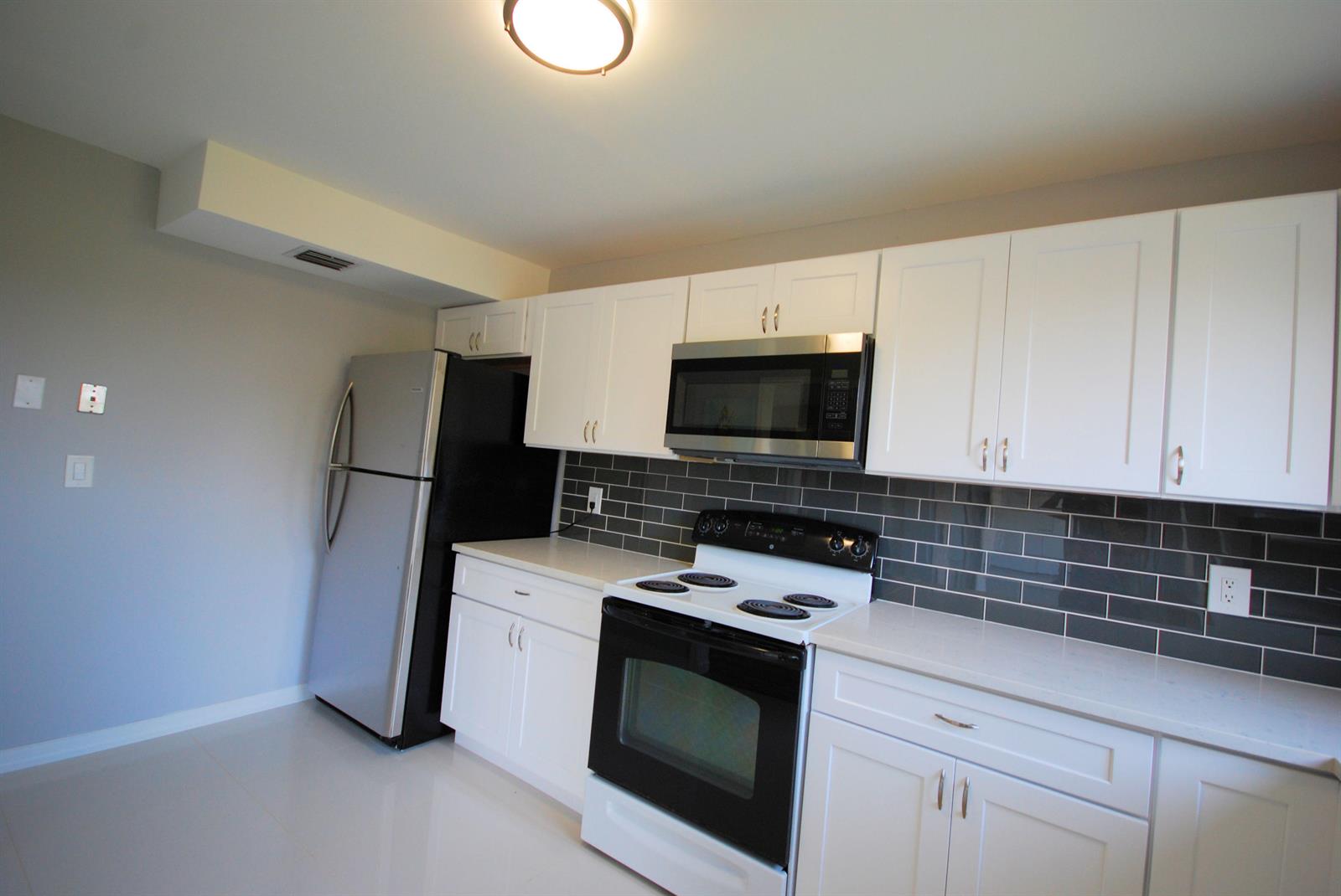 A kitchen features white cabinets, stainless steel appliances, and a dark gray subway tile backsplash — 5917 Via Vermilya # 308, Lake Worth FL 33462, LAKE WORTH, FL