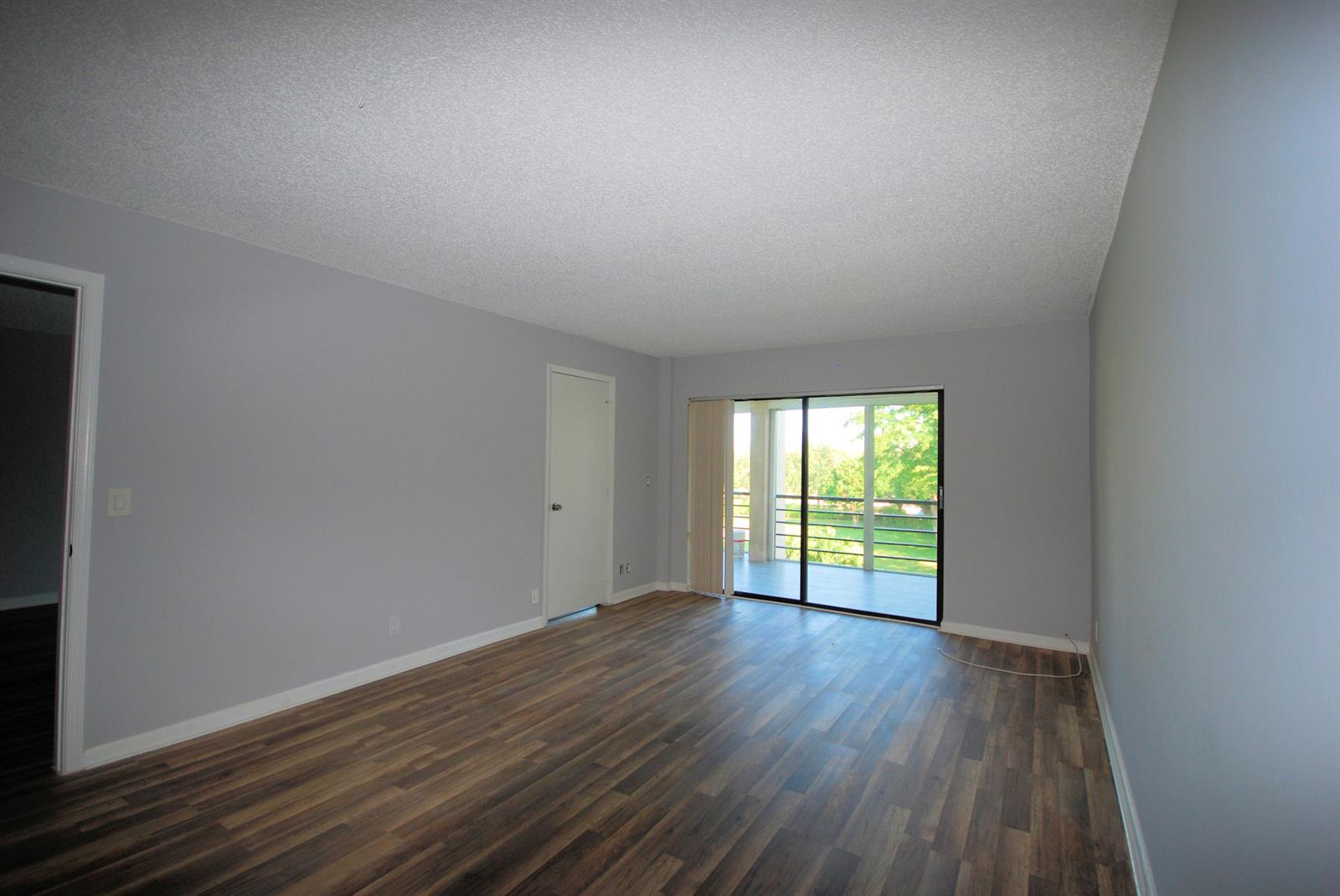 An empty living room with gray walls, wood-look flooring, and a sliding door to a balcony — 5917 Via Vermilya # 308, Lake Worth FL 33462, LAKE WORTH, FL